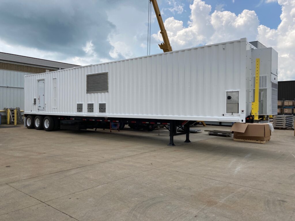 A towable hybrid charging unit sitting in a parking lot near a warehouse